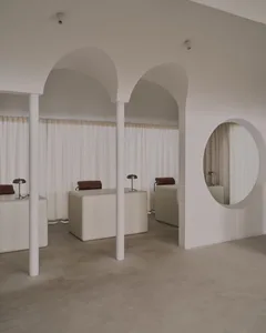 A modern hair salon with white walls, a circular mirror, and two chairs in front of it, with soft and diffused lighting creating a relaxing atmosphere