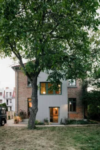 A well-maintained brick house with metal accents and a tree in front, creating a warm and welcoming atmosphere
