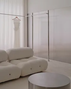 A modern living room with a white couch and chair, a mirror, and a dress on a rack, with soft and diffused lighting creating a warm atmosphere
