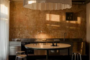 A modern kitchen with a round marble table and stools, sink, and oven, lit dimly for a cozy atmosphere