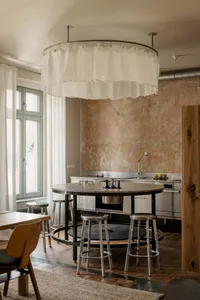 Residential kitchen with a wooden floor, white walls, and a dining table surrounded by chairs, with a sink and oven, in a dimly lit space
