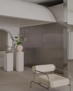 A living or dining area with a white chair, a vase, and a potted plant, surrounded by a mirror that reflects the room's interior