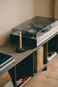 A black and white photograph of a cozy living space with a record player and candle on a table, surrounded by a bookshelf and a couch