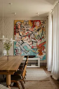 Dining room with a wooden table, brick walls, and a colorful painting above the table