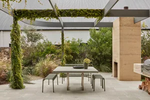 A well-lit outdoor patio with a dining table, chairs, and a vase with flowers, surrounded by a stone wall and a fireplace in a garden setting