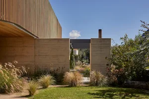 A modern house with a concrete exterior, a large window, and a patio area surrounded by greenery
