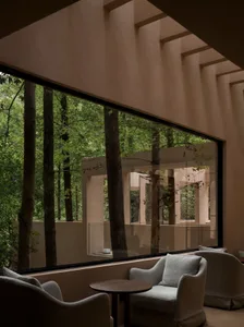 Cozy living room with a couch, chair, and dining table, surrounded by a forest view through a large window