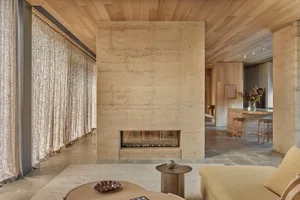 Cozy living room with a stone fireplace, a couch, a chair, and a dining table, well-lit by natural light through windows