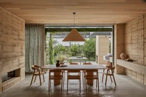 A modern dining room with a wooden table and chairs, surrounded by a large window and a kitchen in the background, with a clean and minimalist design