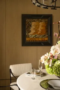 Dining room with a wooden floor, a dining table, chairs, a vase of flowers, and a painting on the wall