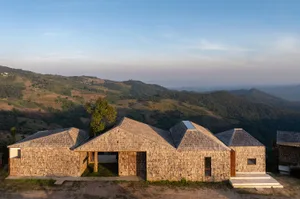 Photograph of a serene hillside house with a triangular shape, blending modern and traditional architecture, featuring a large window and natural light