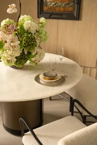 Dining room with a wooden floor, a black table and chairs, and a white tablecloth, set with a vase of flowers and wine glasses