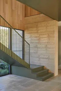 A residential staircase with green railings, a stone wall, and a window, set in a warm and inviting atmosphere