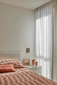 Cozy bedroom with a bed, dresser, and natural light from a window, featuring a white color scheme and plaid blanket