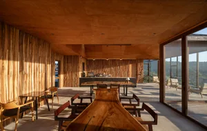 Warm and inviting dining space with a wooden table, chairs, and walls, surrounded by natural sunlight