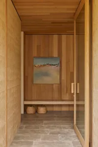 A modern bathroom with a wooden door and a beach scene painting on the wall, featuring a bench and a doorway, with dim lighting creating a cozy atmosphere