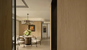 Modern dining room with a wooden floor, a large dining table, and elegant decor including a chandelier, vase, and potted plant