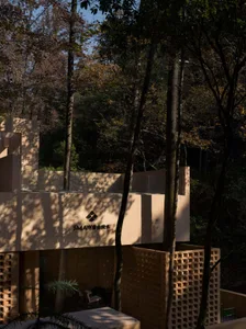Photograph of a modern building with a curved structure, surrounded by trees, featuring a tan exterior and wood accents, with natural light and a serene atmosphere