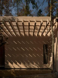 A photograph of a house with a wooden structure and a shaded area under a tree, creating a cozy atmosphere