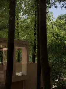 A serene modern building with a glass wall surrounded by trees, blending with its natural environment
