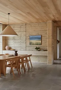 A modern kitchen with a dining table and chairs, surrounded by a counter with a vase, featuring wood and stone materials in a well-lit space