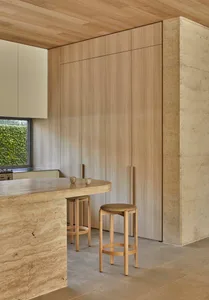A modern kitchen with wooden cabinets, a marble countertop, and a dining table with chairs, featuring soft and warm lighting