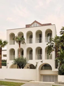 A large white building with a modern architectural style, featuring a large archway and balcony, with natural light illuminating the structure