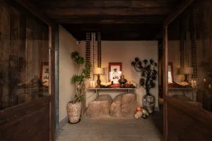 Cozy living space with a wooden floor, stone walls, a rock wall, and dim lighting, featuring a stone bench, potted plant, and decorative vases