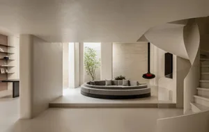A modern living room with a circular couch, a potted plant, and a vase, set against a backdrop of white walls and well-lit for a comfortable atmosphere
