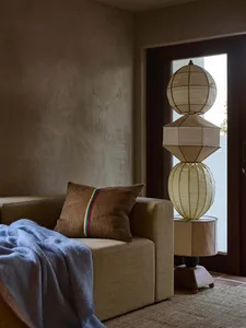 Cozy living room with a brown sofa, a wooden chair, a metal lamp, and a doorway in the background, dimly lit