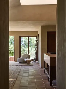 Cozy modern living space with a stone floor, a large window, and a stone wall, featuring a couch, chair, and dining table, with dim lighting and natural materials