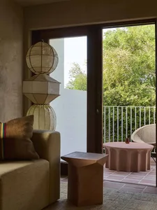 Modern living room with a couch, chair, dining table, and various decorative items, featuring wood and glass materials and natural light from a window