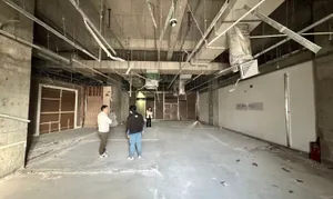 A large, empty room with a cement floor, a crane in the background, and a dim, moody atmosphere