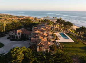 A large beach house with a Spanish-style architecture, surrounded by trees and featuring a pool and a living room, dining room, and backyard with a pool