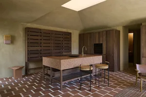 A modern kitchen with a wooden counter, tile floor, and white refrigerator, lit by natural sunlight through a window