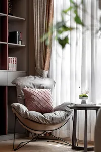 Cozy modern living space with a chair, table, and potted plant, surrounded by a couch and bookshelf, with natural light from the window