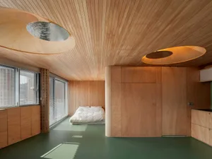 Warm and inviting bedroom with wooden walls and floor, natural light from windows, and a bed in the center of the room