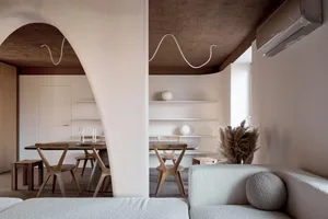 Cozy living room with a couch, dining table, chairs, and potted plant, featuring a mix of natural and artificial lighting