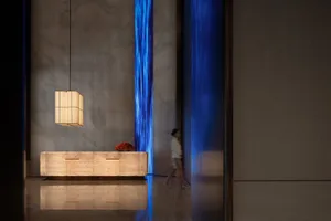 Modern lobby with a blue wall, a wooden desk, and a blue light fixture, featuring a woman walking past the desk