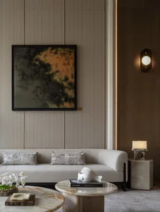 A well-lit living room with a white couch, a chair, and a large painting on the wall, accompanied by a vase on a table