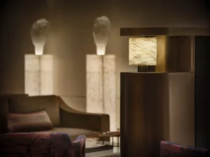 Cozy living room with a modern style, dim lighting, and wooden furniture, including a couch, chair, and lamp, with decorative accents like a vase and bowl