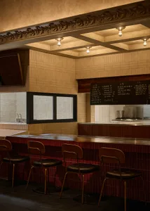 Modern restaurant interior with a wooden bar, brick wall, and tile floor, featuring a counter and chairs, with lights on the ceiling