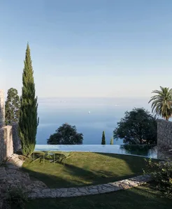 A serene outdoor patio with a stone floor, a swimming pool, a dining table, and chairs, surrounded by a beautiful landscape