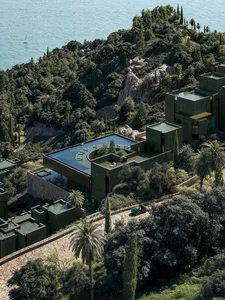 Modern building with a green roof, surrounded by a lush hillside and a body of water, featuring a mix of traditional and contemporary architectural styles, with concrete, glass, and wood materials, and natural lighting