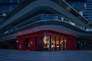 A modern restaurant with a red brick facade, featuring a large window and a cozy interior with chairs and dining tables