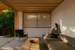 A well-lit living room with a woman reading on a couch, surrounded by wooden furniture and a warm atmosphere