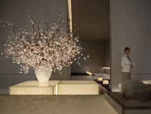 A modern lobby with marble table and floor, featuring a large white vase with white flowers and several potted plants
