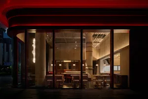 A modern restaurant interior with dining tables, chairs, and benches in a neutral color palette, with warm and soft lighting