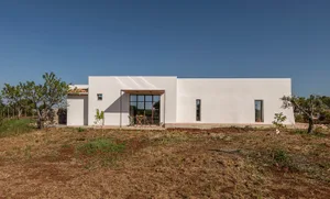 A modern house with a white exterior, surrounded by a grassy area, with a large patio and architectural details visible