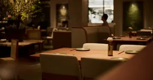 A calm and inviting restaurant with a wooden table and chairs, set with plates and a vase, in an empty space
